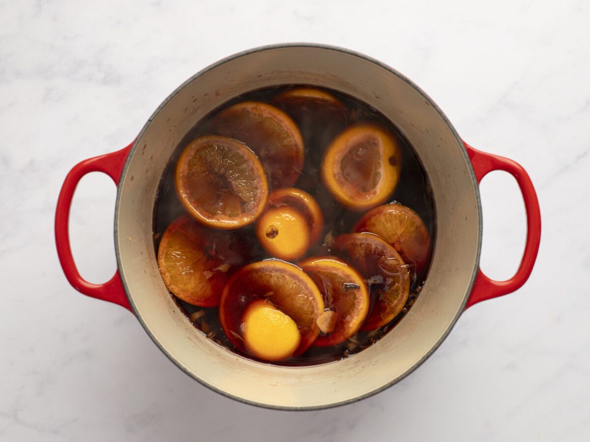 Simmering wine, orange slices, brandy, honey, sugar, cinnamon, cloves, star anise, and ginger in a large saucepan.