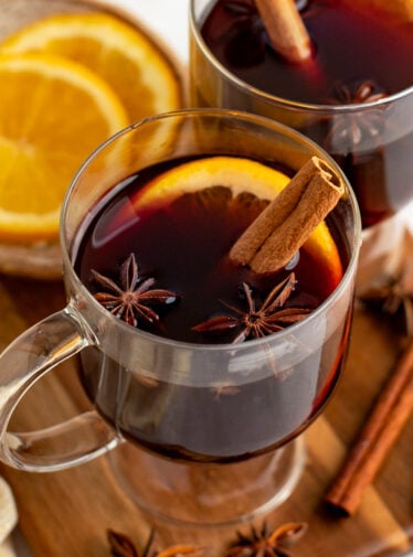 mugs of mulled wine with cinnamon sticks, orange slices and spices.