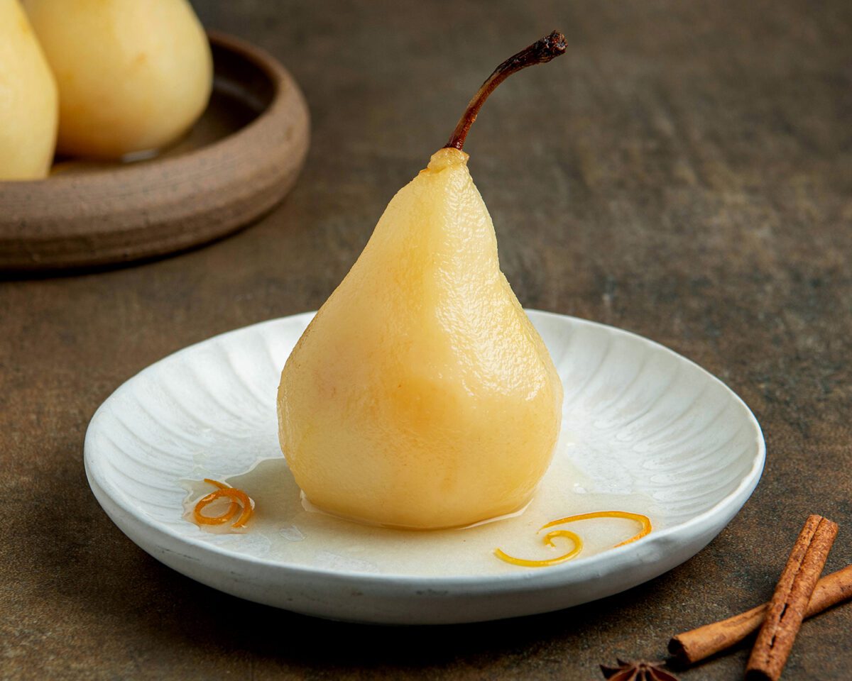 poached pear garnished with citrus peels on white plate with syrup