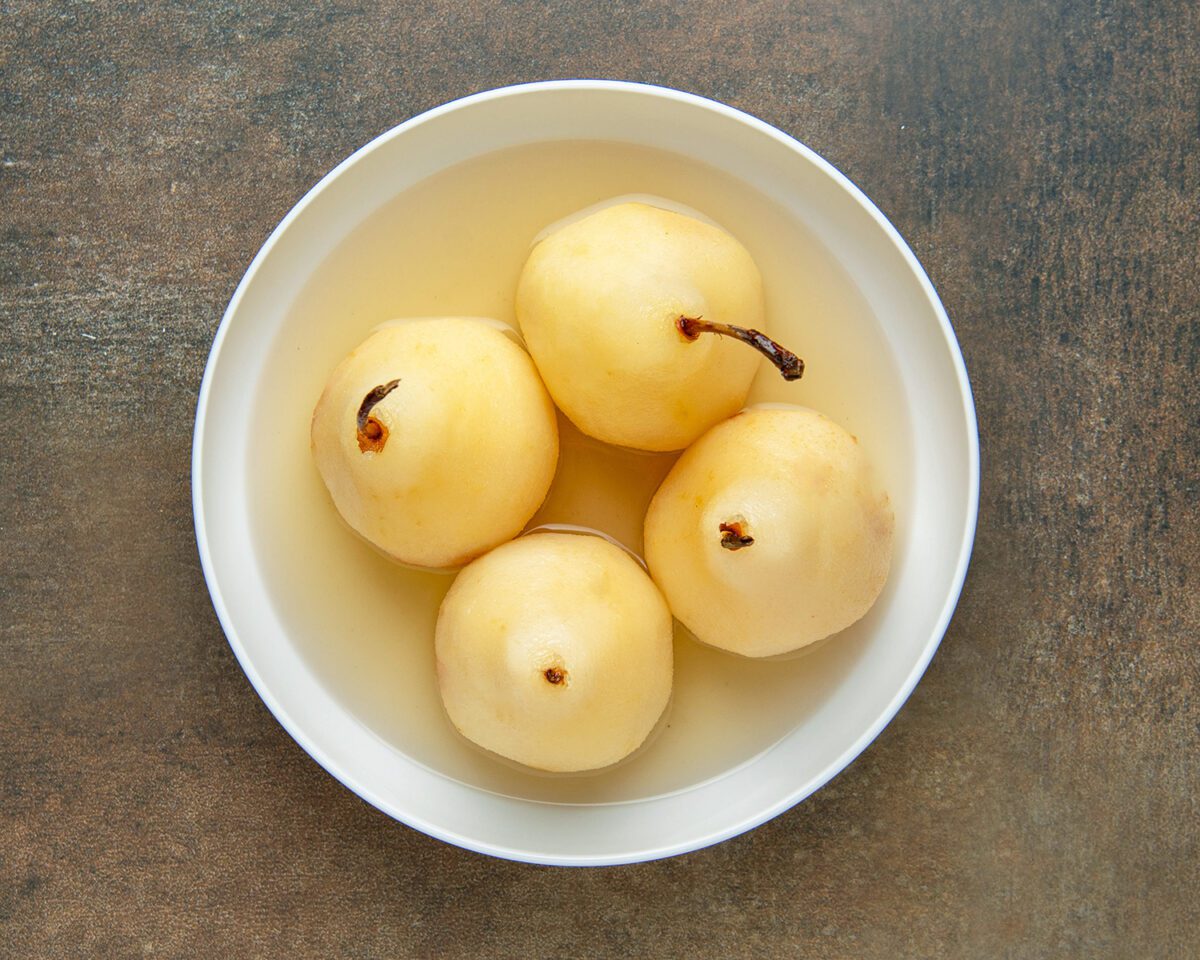 poached pears in white bowl with syrup