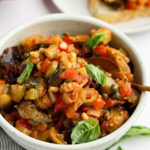 white bowl with caponata with baguette slices topped with caponata nearby