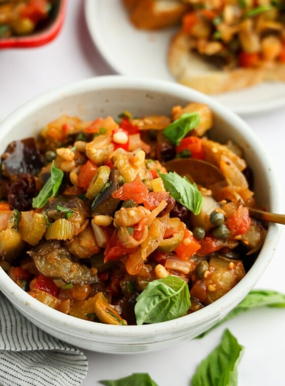white bowl with caponata with baguette slices topped with caponata nearby