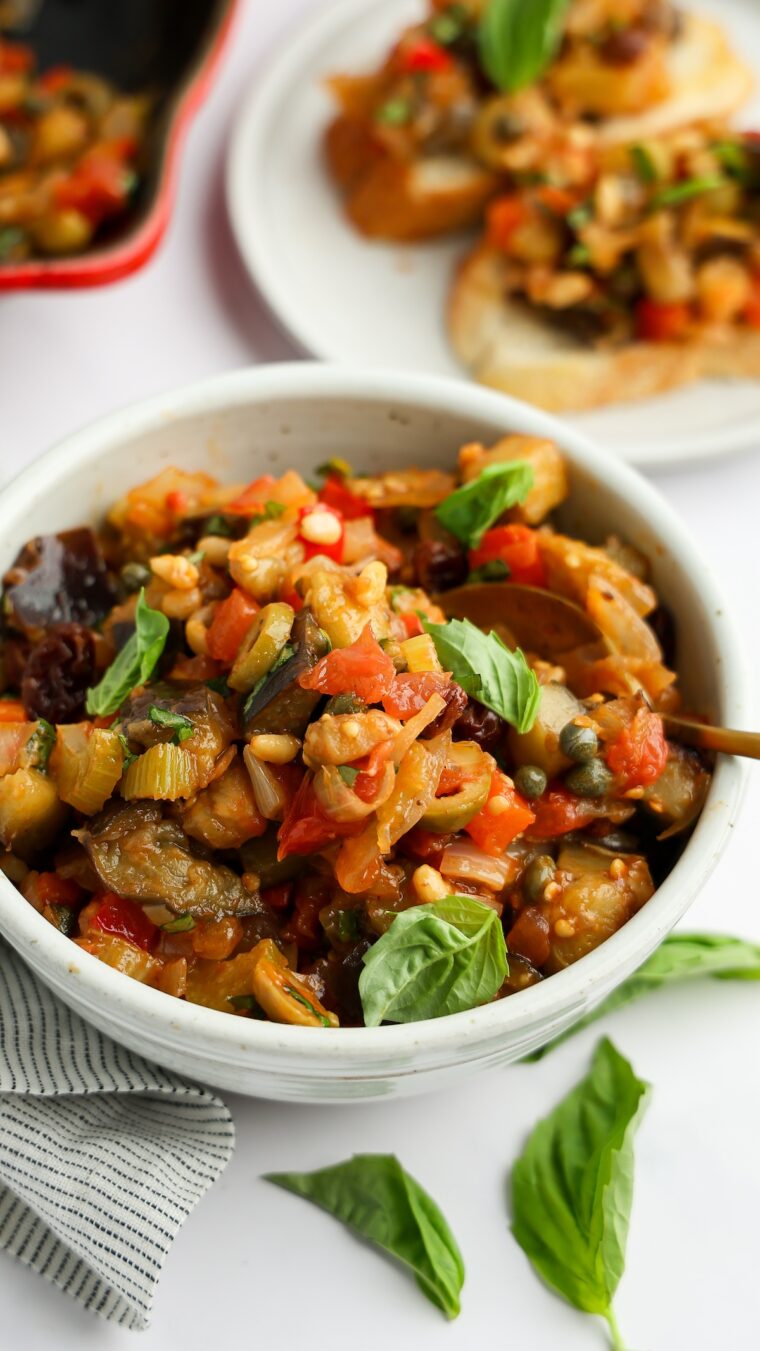 white bowl with caponata with baguette slices topped with caponata nearby