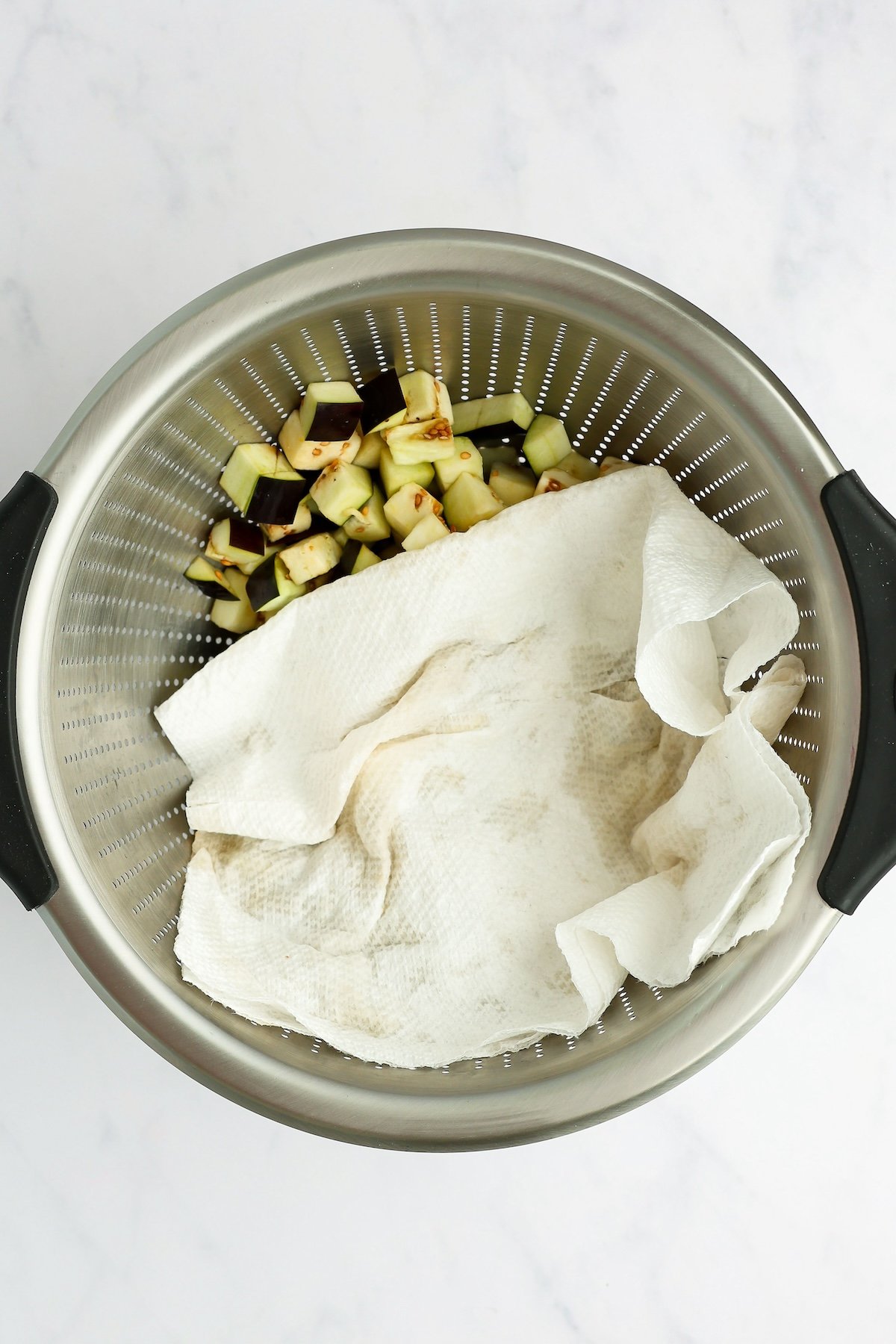 paper towels patting eggplant dry in colander
