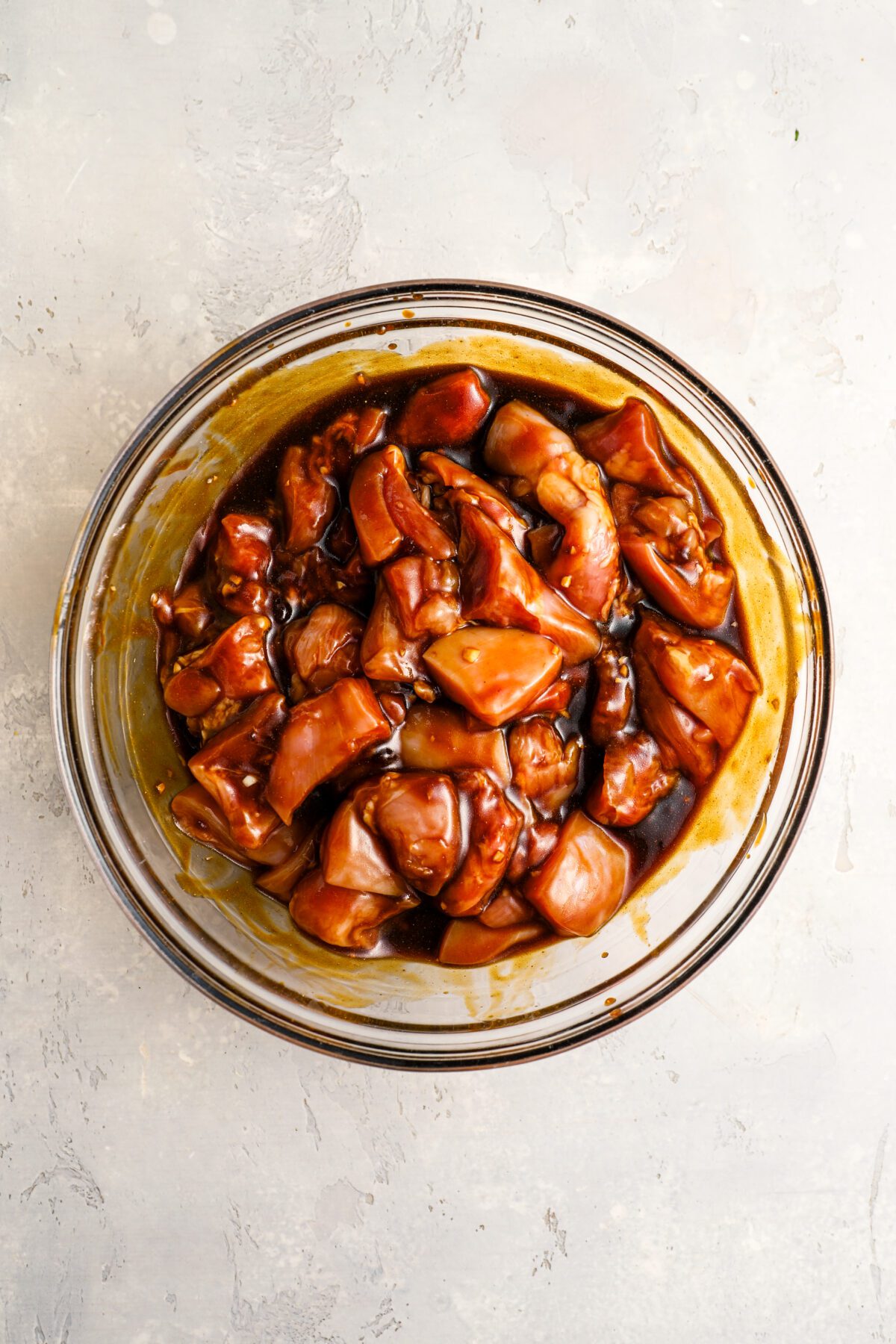 large glass bowl with soy sauce, oil, brown sugar, ketchup, garlic, turmeric, and coriander mixture evenly coating chicken