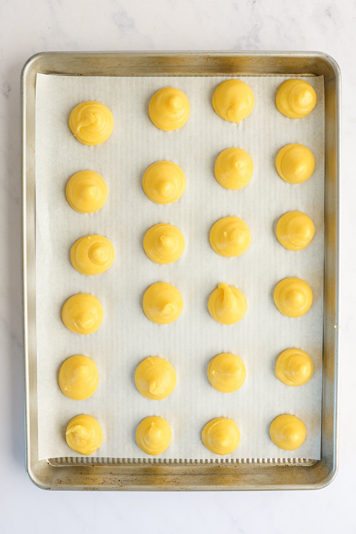 pastry mounds on parchment-lined baking sheet with dough tips pressed down.