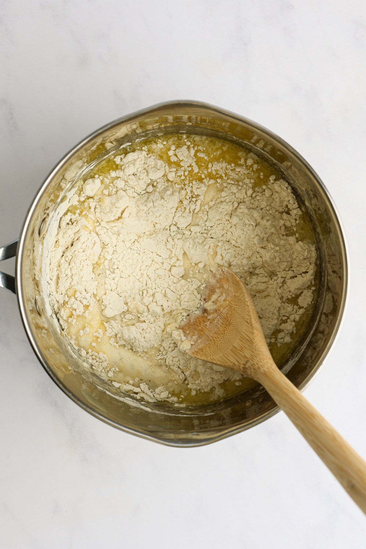 wood spoon stirring water, milk, butter, sugar, salt, and flour in medium saucepan