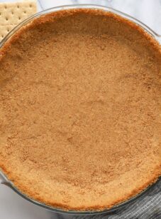 finished graham cracker crust with graham crackers, butter and sugar nearby