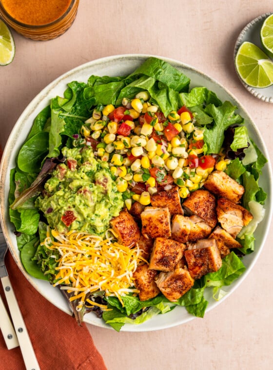 Copycat chipotle chicken in bowl with greens, corn salsa, guacamole and cheese.
