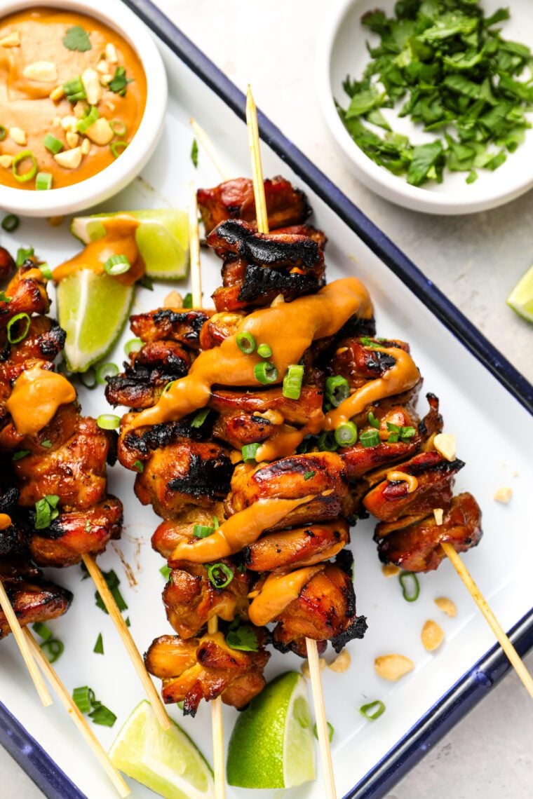 white serving platter with cooked chicken skewers and small bowl of peanut sauce
