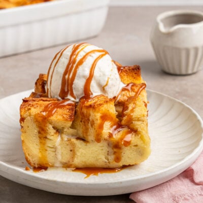slice of bread pudding on plate topped with vanilla ice cream and caramel sauce