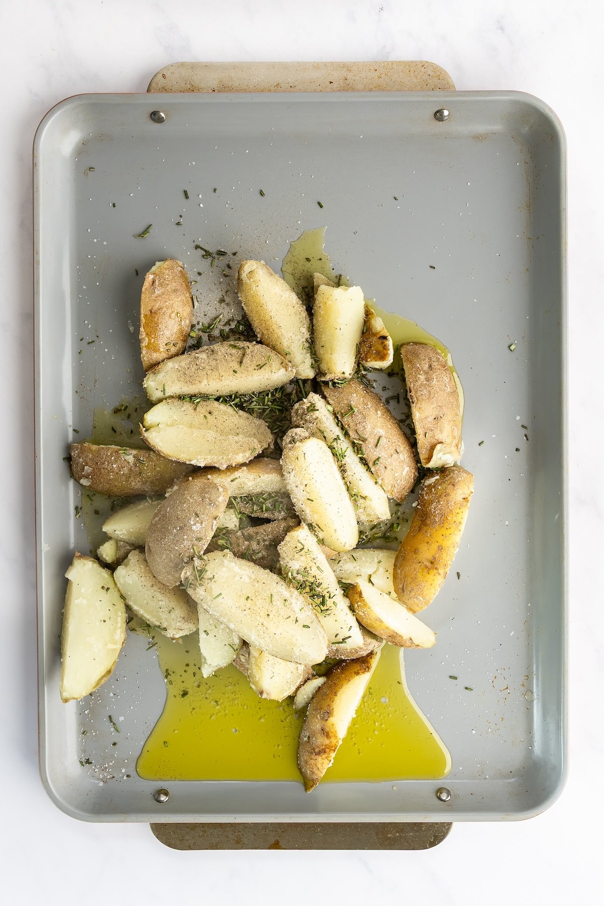 sheet pan with potato wedges, salt, pepper, and rosemary  