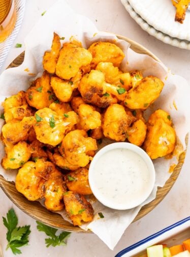 buffalo cauliflower bites in napkin lined basket with ramekin of blue cheese dressing