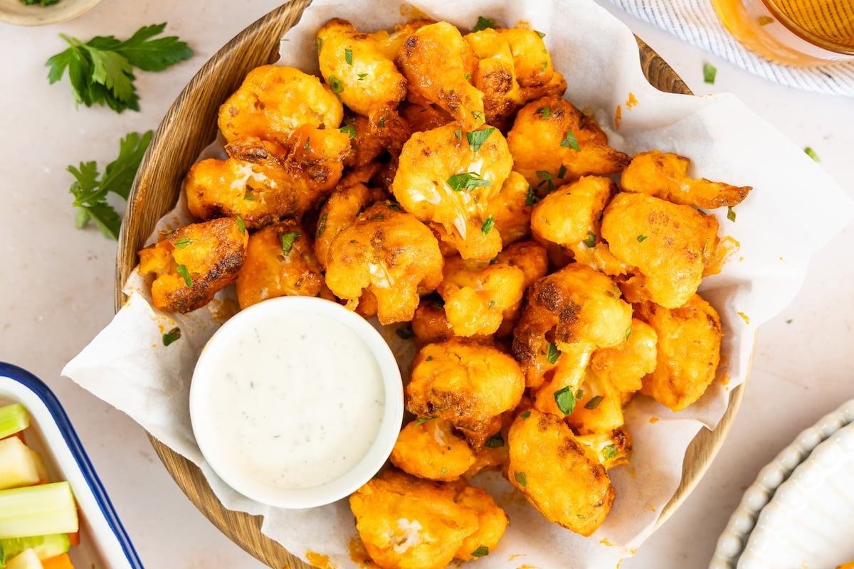 buffalo cauliflower bites in napkin lined basket with ramekin of blue cheese dressing