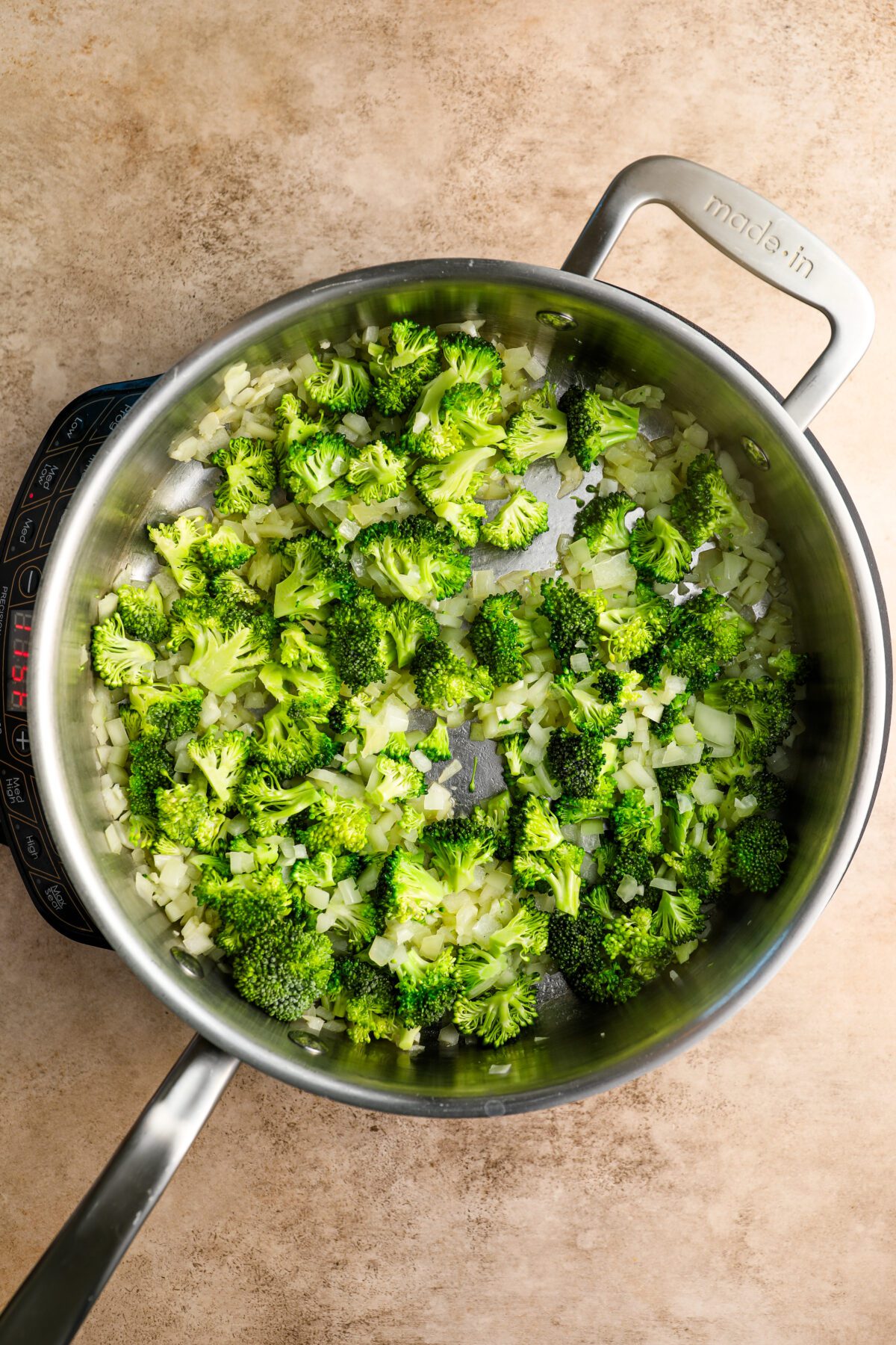 large skillet with onion, garlic, and broccoli florets