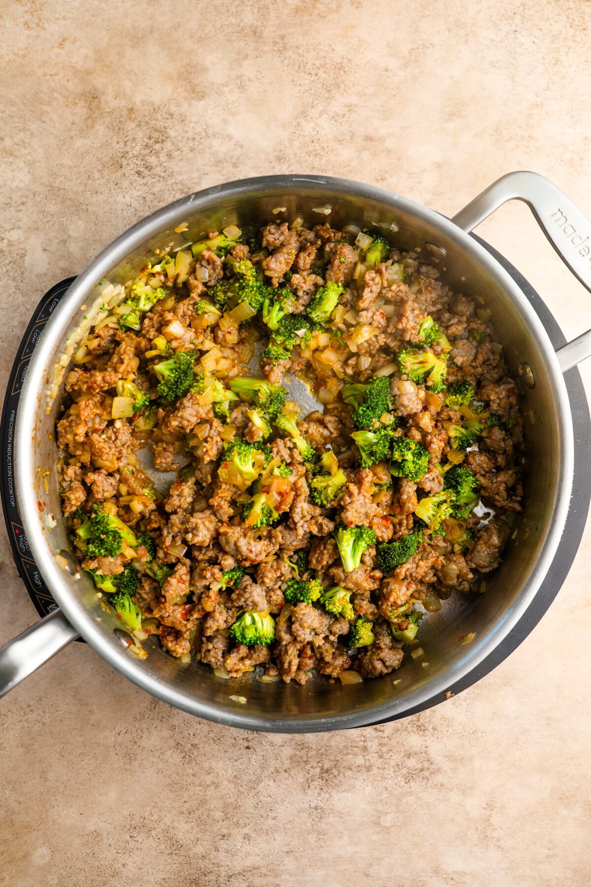 large skillet with onion, garlic, broccoli florets, and cooked sausage