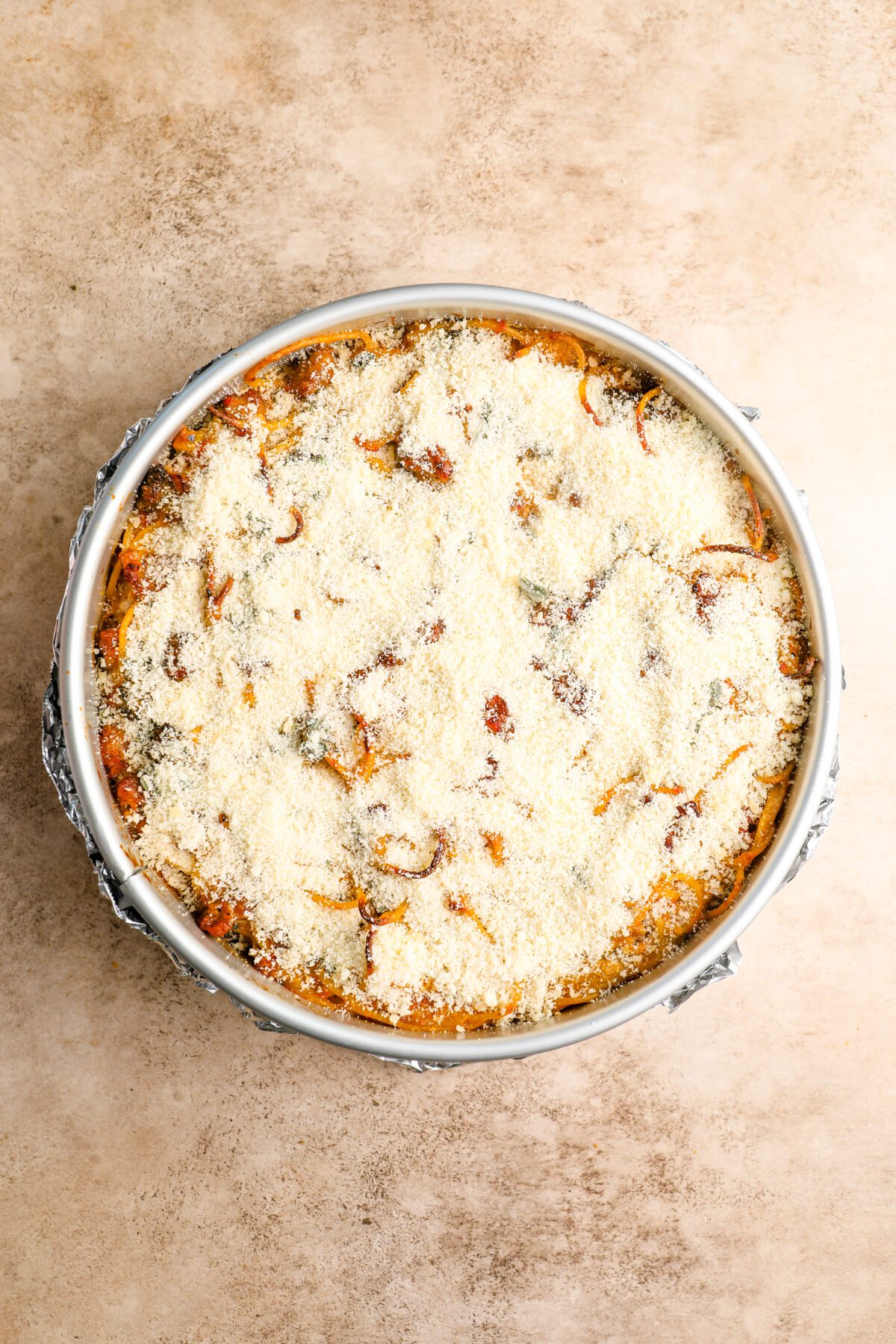 springform pan with baked spaghetti pie topped with parmesan