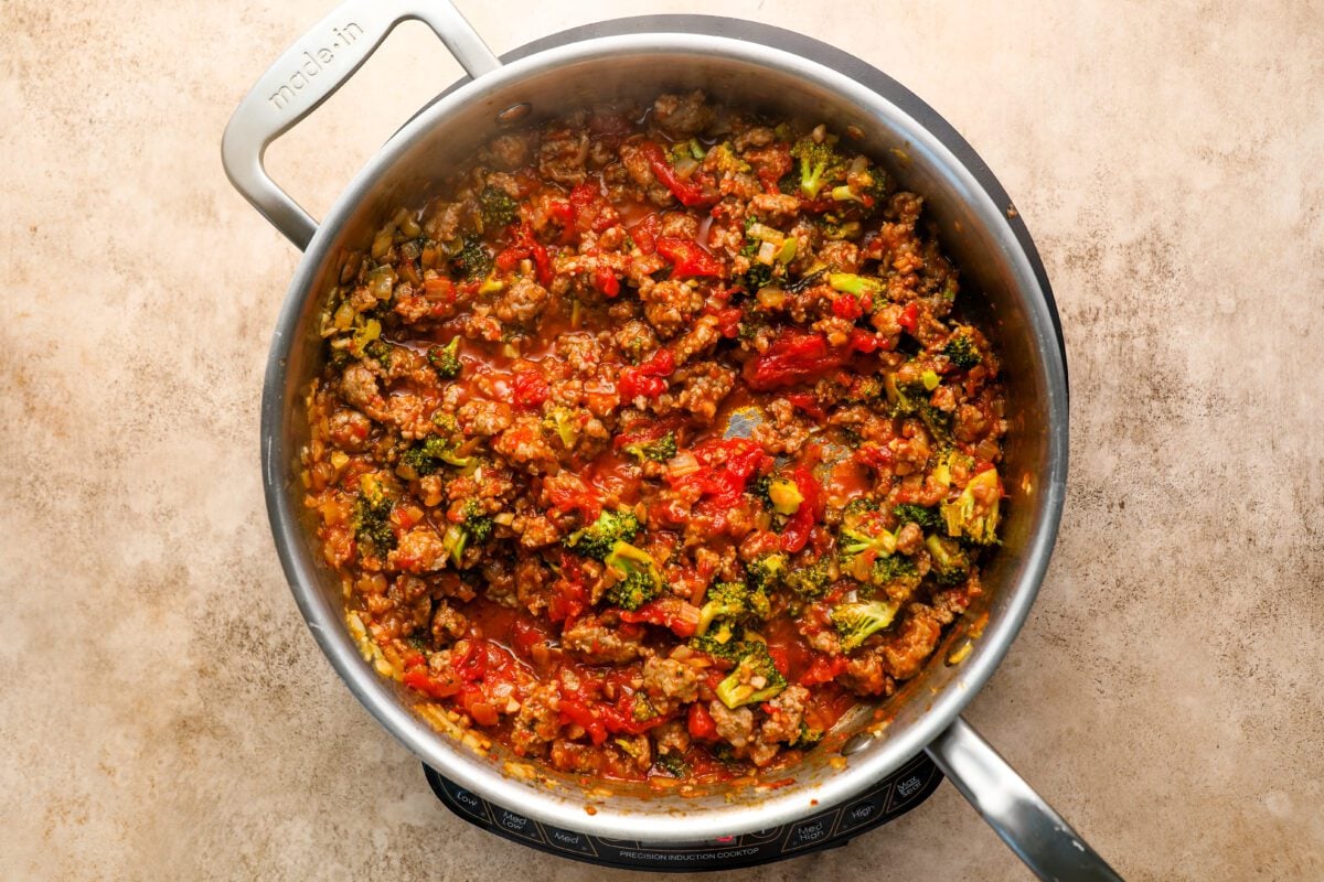 large skillet with onion, garlic, broccoli florets, cooked sausage, and canned tomatoes