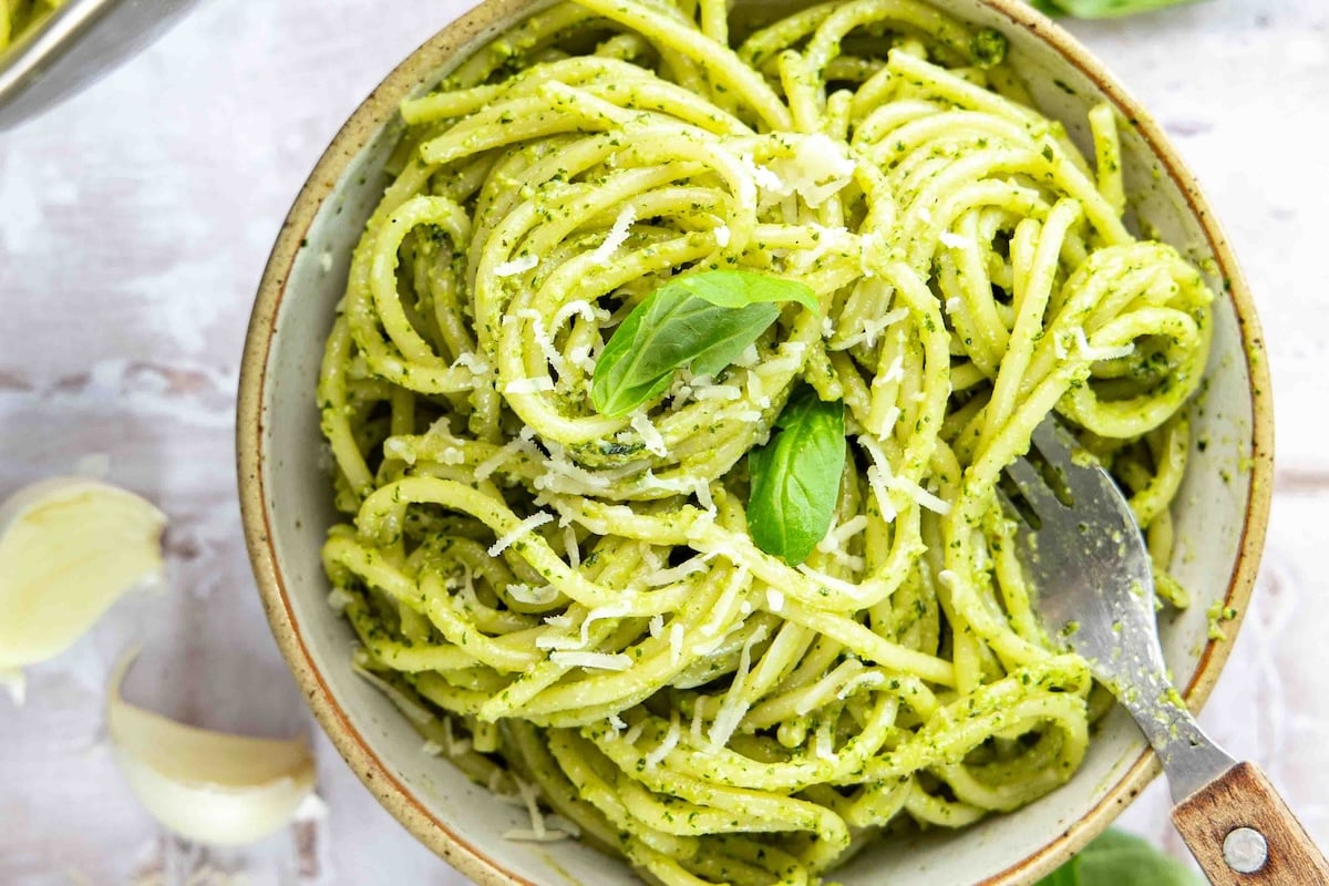 bowl with pesto pasta garnished with Parmigiano-Reggiano and fresh basil