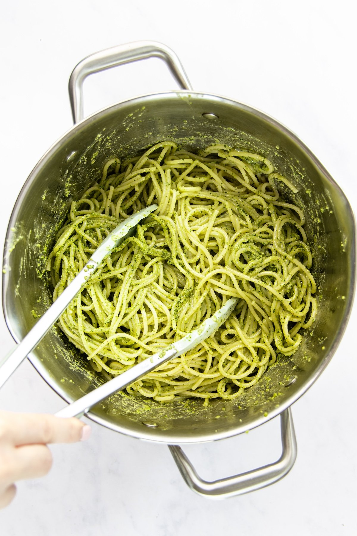 tossing pasta and pesto with tongs