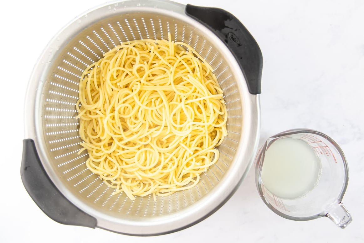 cooked spaghetti in strainer with reserved water in measuring cup