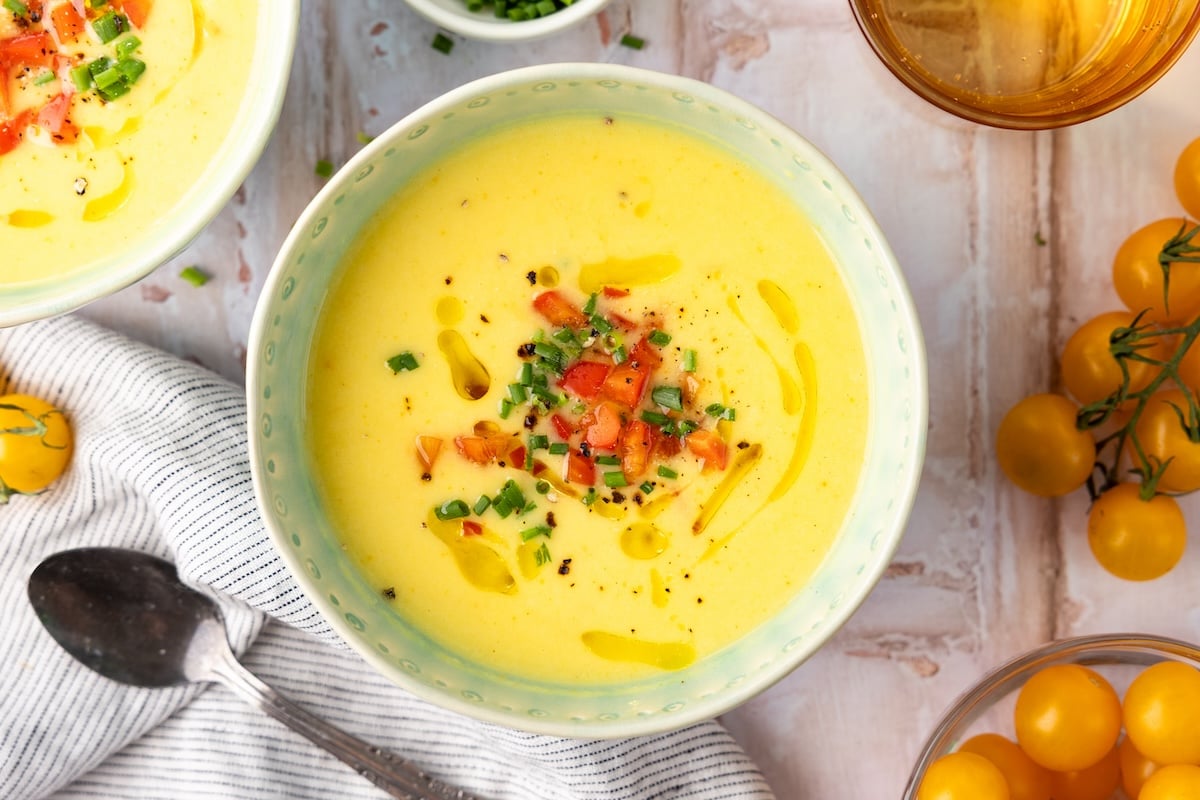decorative soup bowl with golden gazpacho garnished with red bell pepper, minced chives, and splash of olive oil