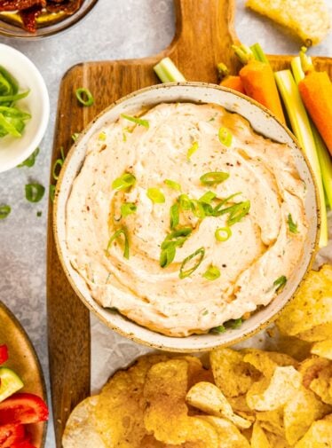 Sun-dried tomato dip in serving bowl on wood cutting board