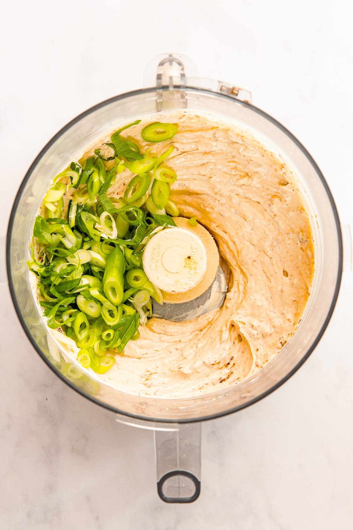 food processor with blended sun-dried tomato dip topped with sliced scallions