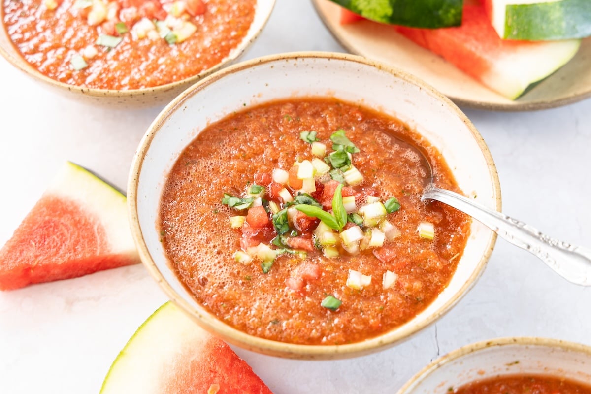 white bowl with watermelon gazpacho topped with chopped watermelon, celery, and basil