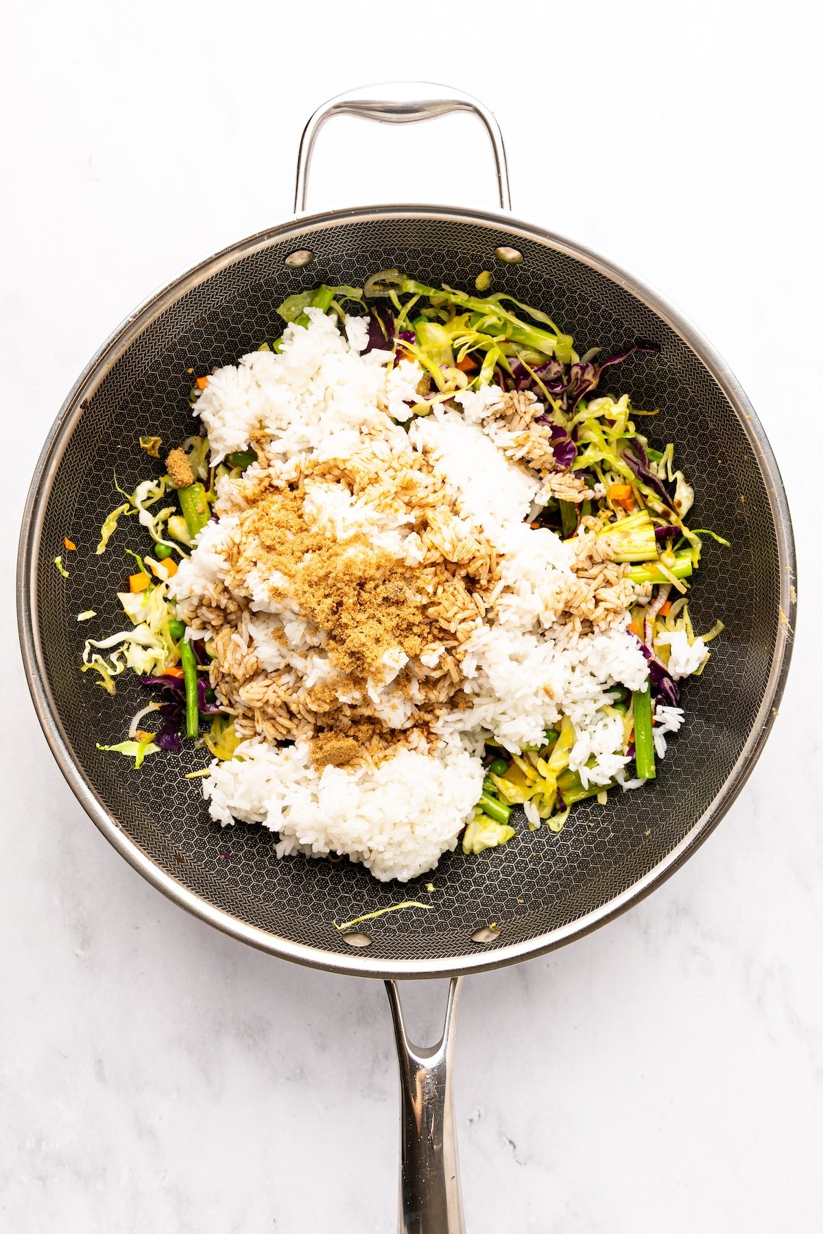 nonstick skillet with rice, soy sauce, fish sauce, and brown sugar piled on top of veggie/aromatic mixture