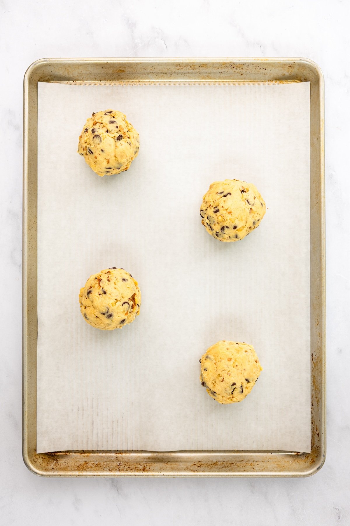 parchment-lined baking sheet with 4 balls of cookie dough