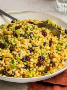 bowl of israeli couscous salad with glass of water and dish of toasted almonds