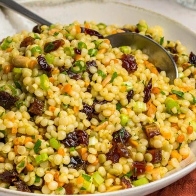 bowl of israeli couscous salad with glass of water and dish of toasted almonds
