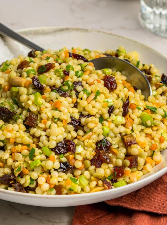 bowl of israeli couscous salad with glass of water and dish of toasted almonds