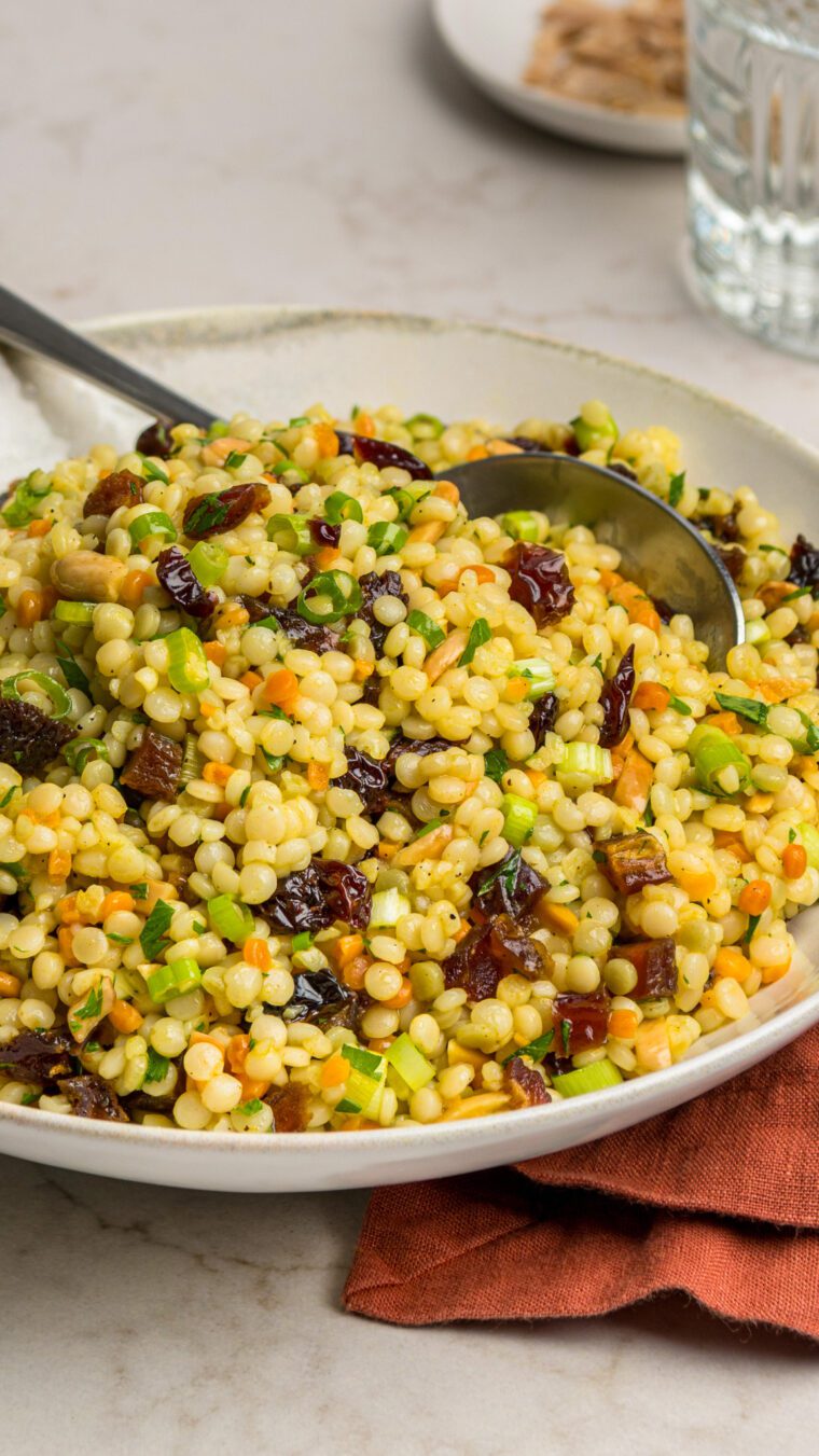 bowl of israeli couscous salad with glass of water and dish of toasted almonds