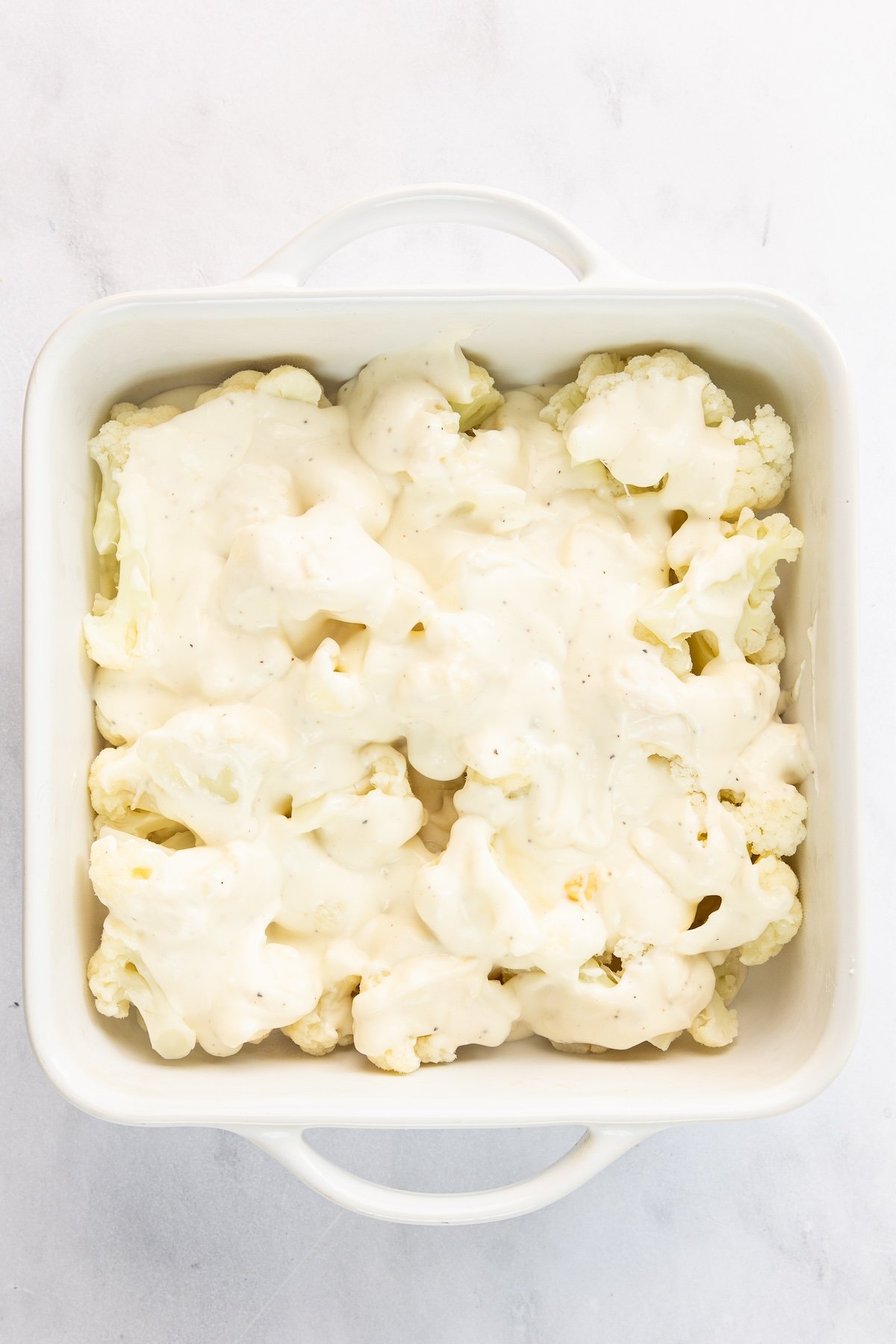 8-inch square baking dish with remaining bechamel sauce spread over cauliflower
