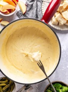 pot of cheese fondue with apple slices, bread cubes, and veggies for dipping