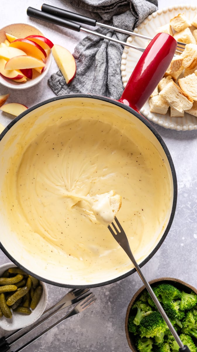 pot of cheese fondue with apple slices, bread cubes, and veggies for dipping