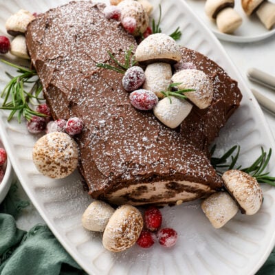yule log cake on platter decorated with meringue mushrooms and sugared cranberries