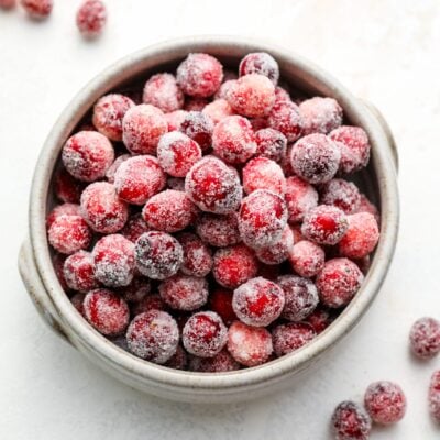 sugared cranberries in white bowl with scattered cranberries surounding bowl