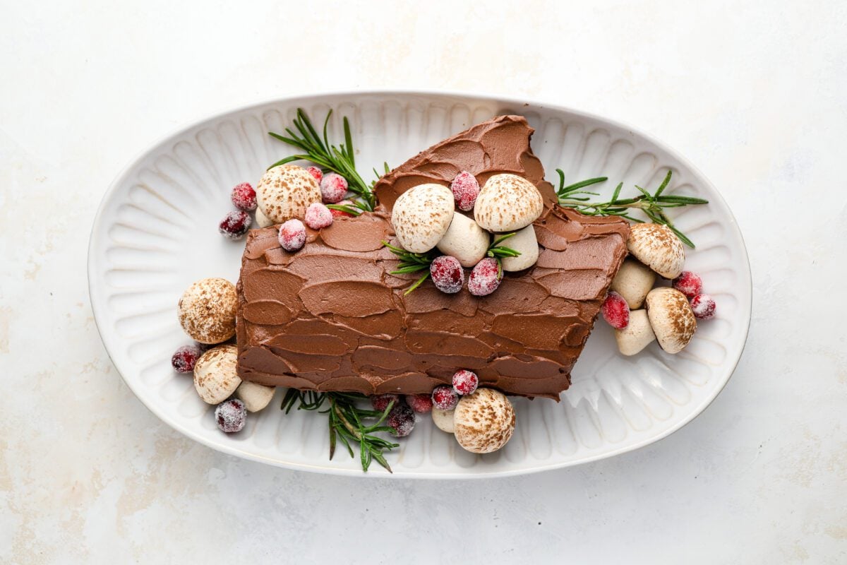 yule log decorated with sugared cranberries, meringue mushrooms, and sprigs of fresh rosemary