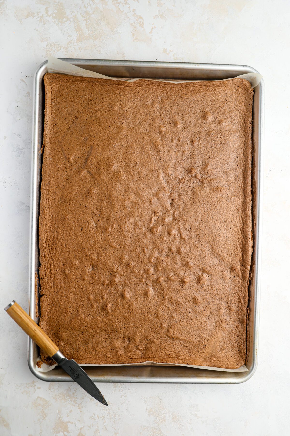 knife separating cake from the edge of jelly roll pan