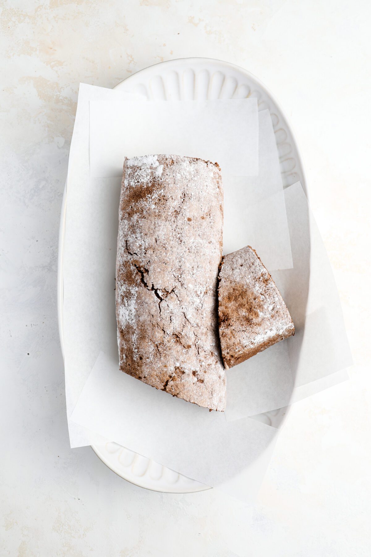 serving platter with diagonal slice of cake placed on side of remaining cake with parchment strips around cake