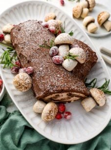 yule log cake on platter decorated with meringue mushrooms and sugared cranberries