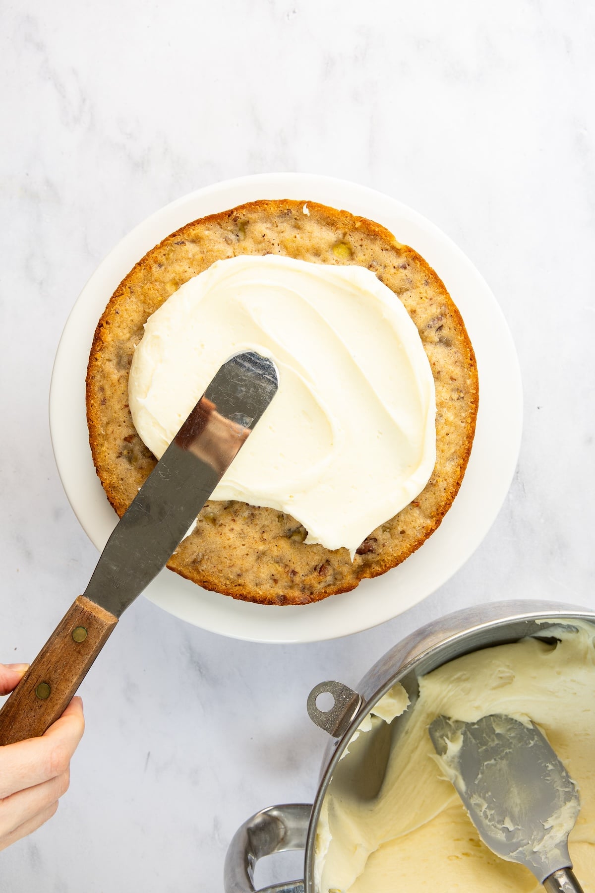 Offset spatula spreading frosting onto bottom layer of cake