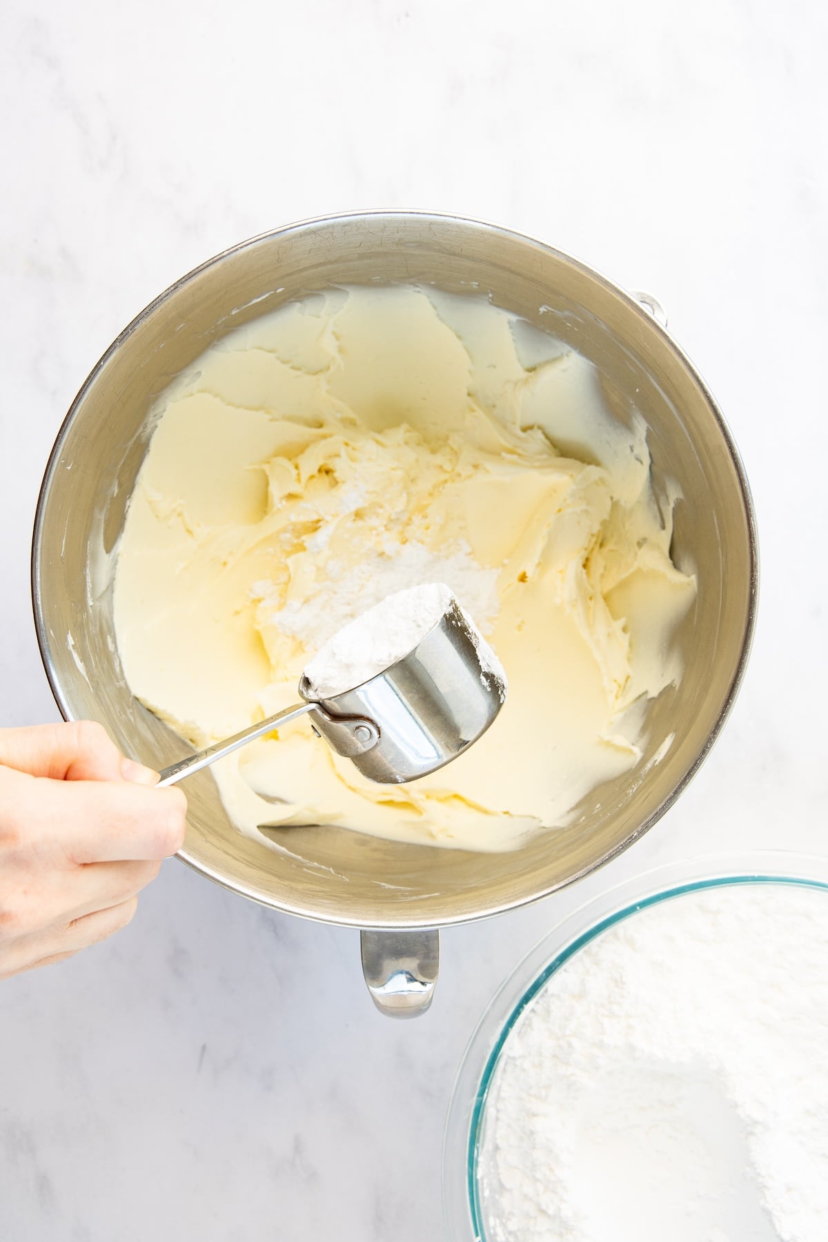 Adding confectioners sugar to mixing bowl with cream cheese, butter, vanilla, and salt