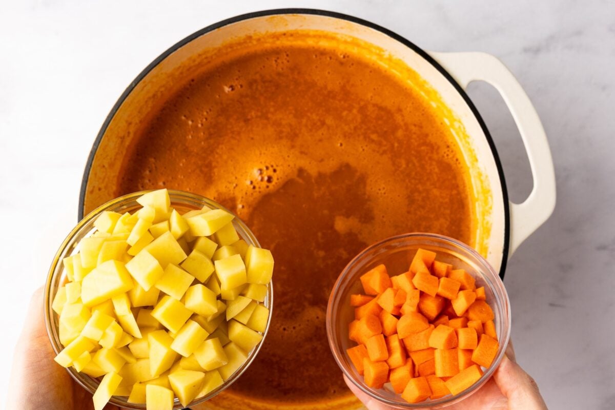 adding carrots and potatoes to albondigas broth in dutch oven