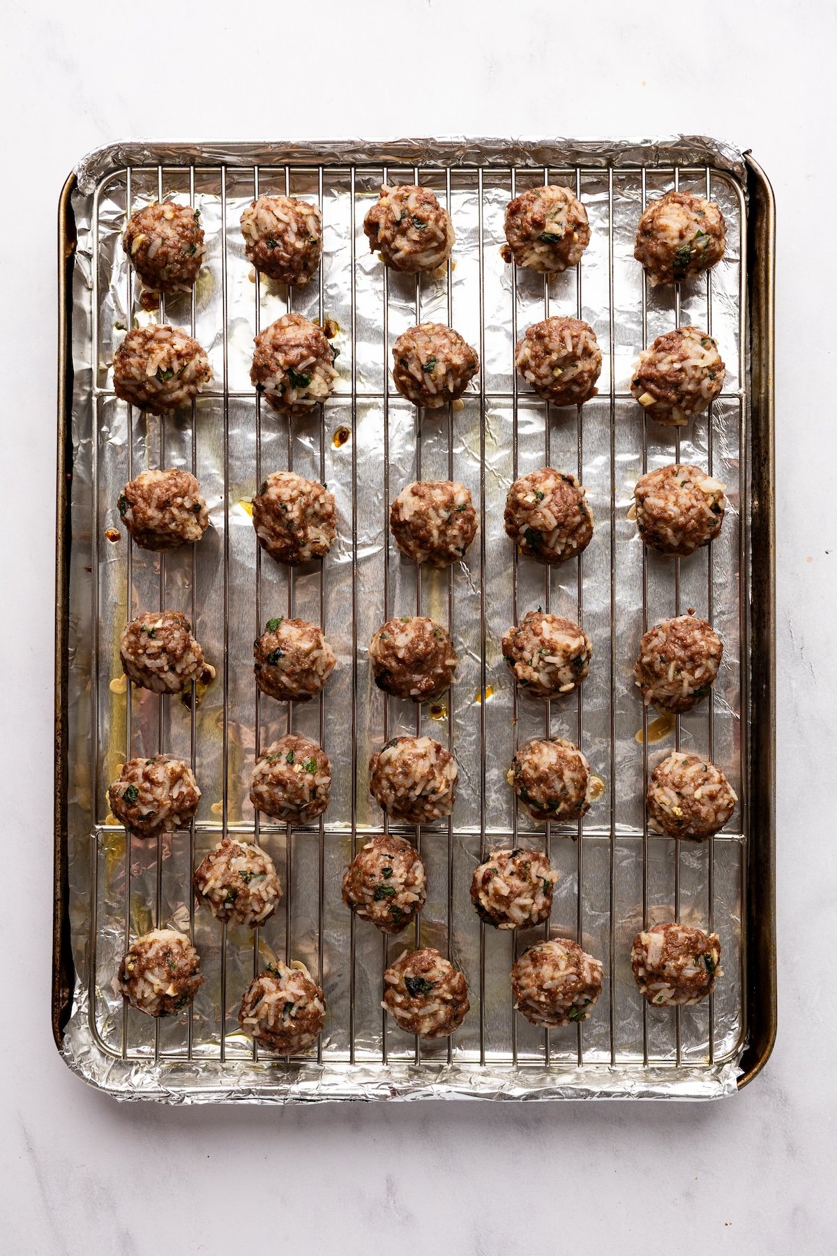 baked meatballs arranged on rack on top of foil-lined baking sheet