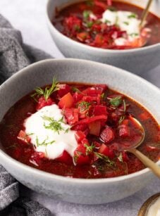 2 bowls of borscht topped with sour cream and fresh dill