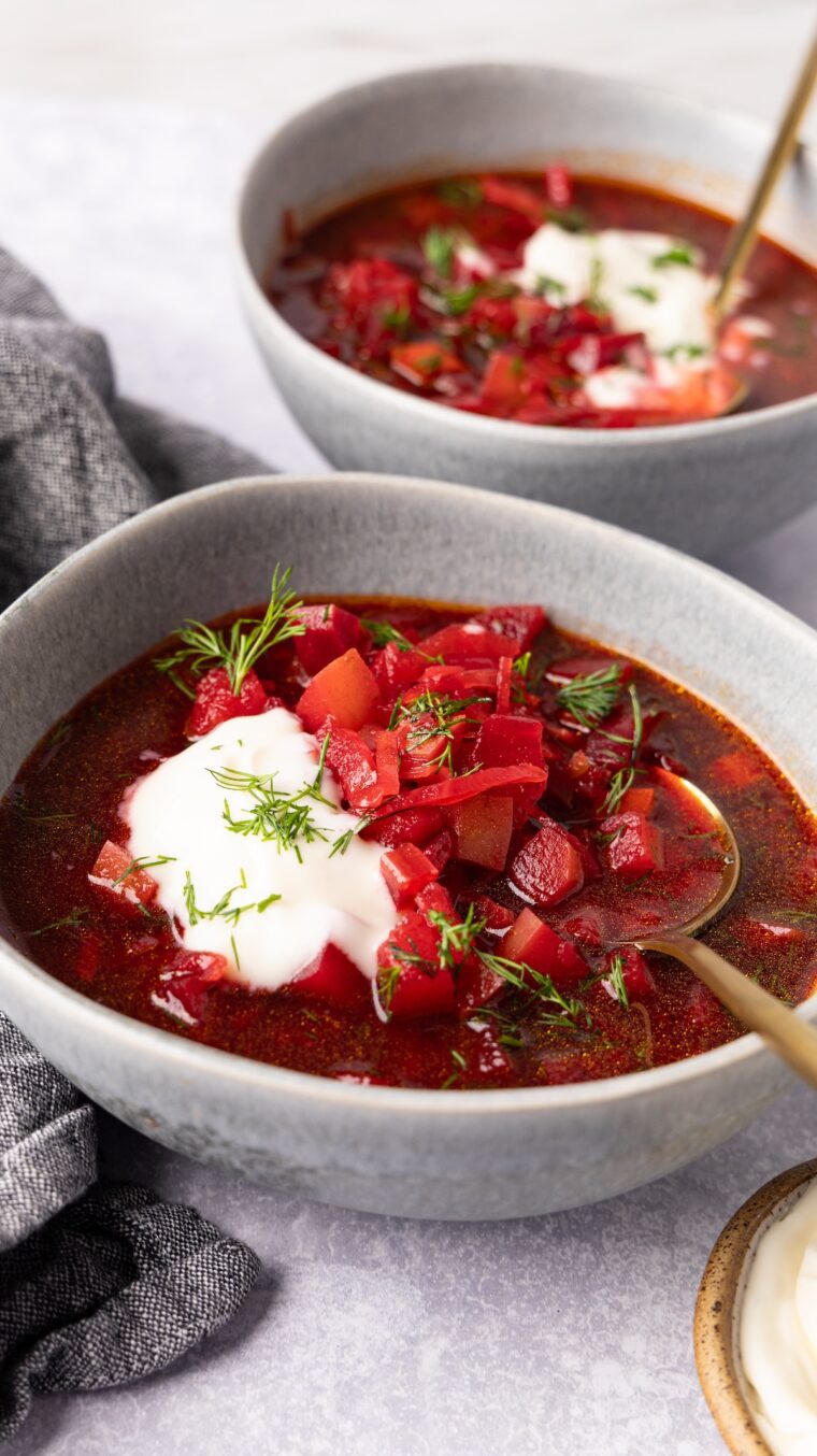 2 bowls of borscht topped with sour cream and fresh dill